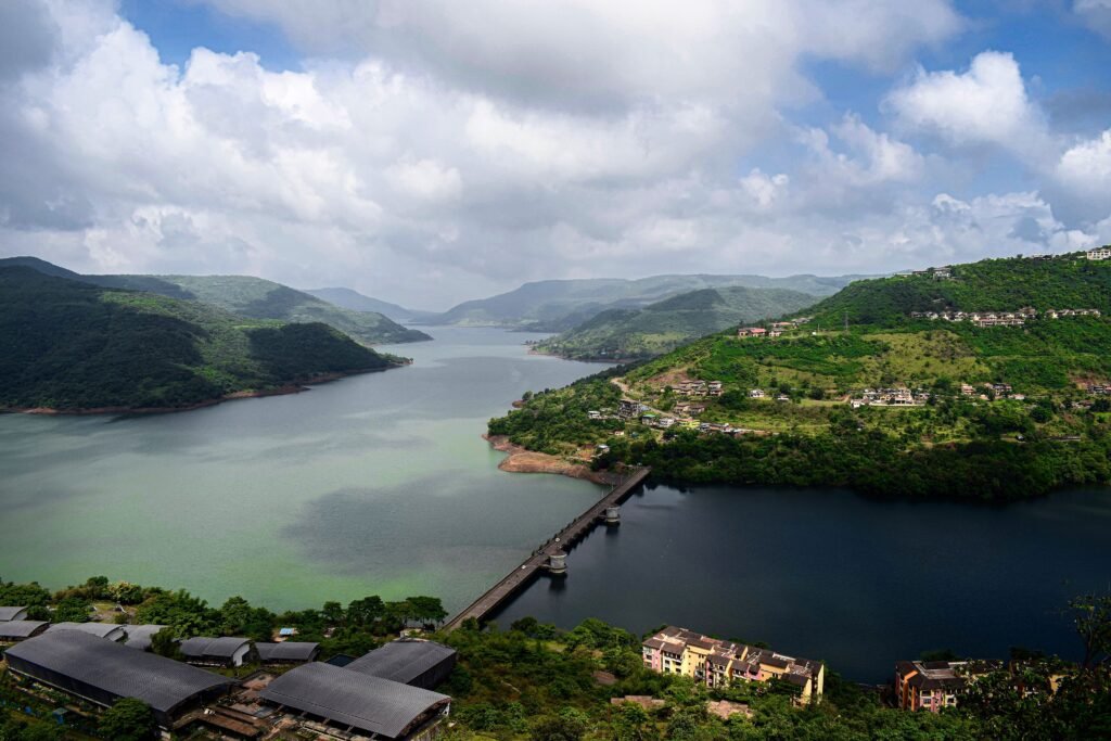 Best Monsoon Road Trips in India. Mumbai/Pune to Mahabaleshwar — The Hill Station Escape. Aerial view showcasing a picturesque bridge crossing a serene river amidst lush green hills.